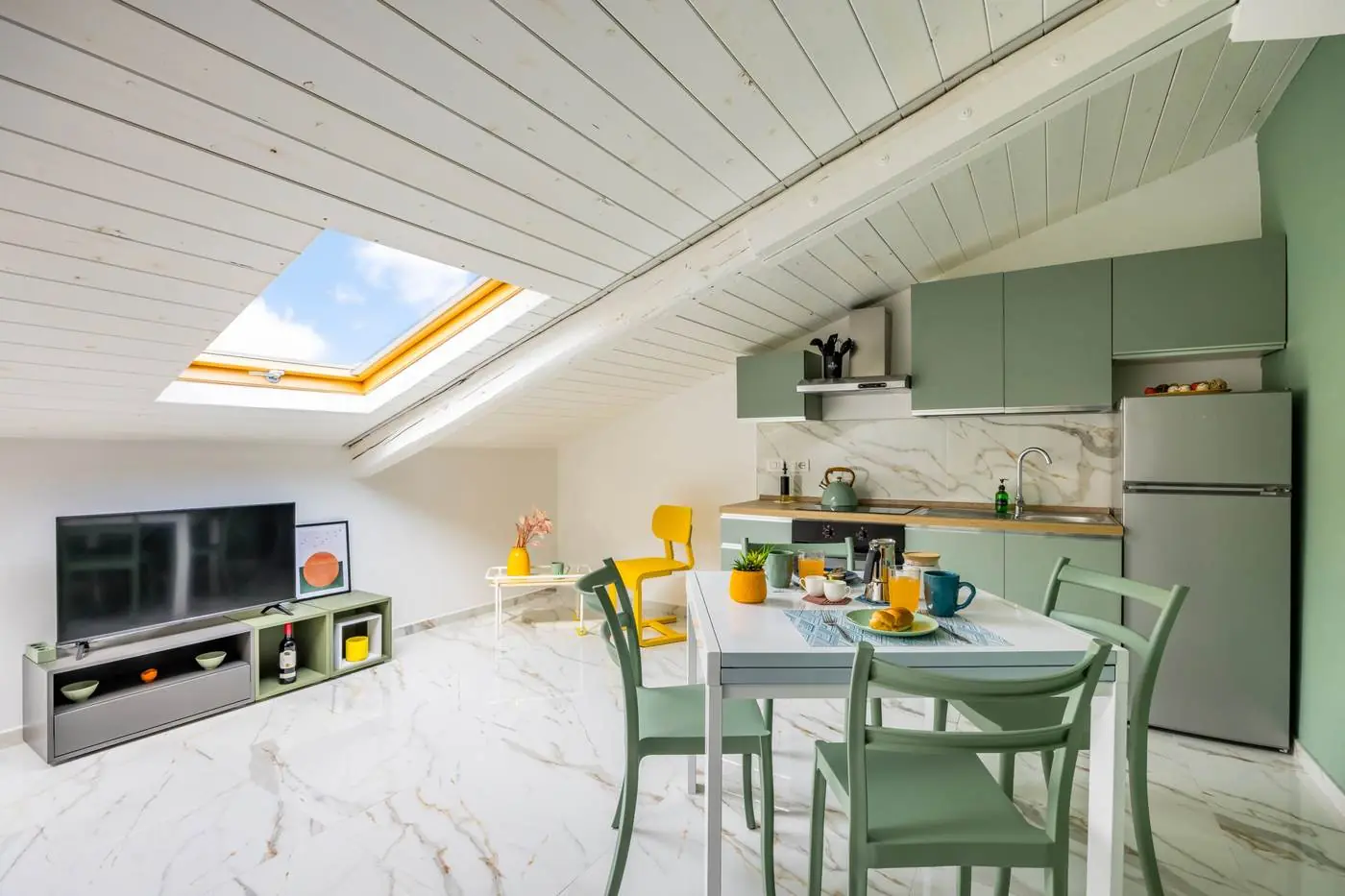 Living open space con lucernario, cucina verde salvia e tavolo da pranzo